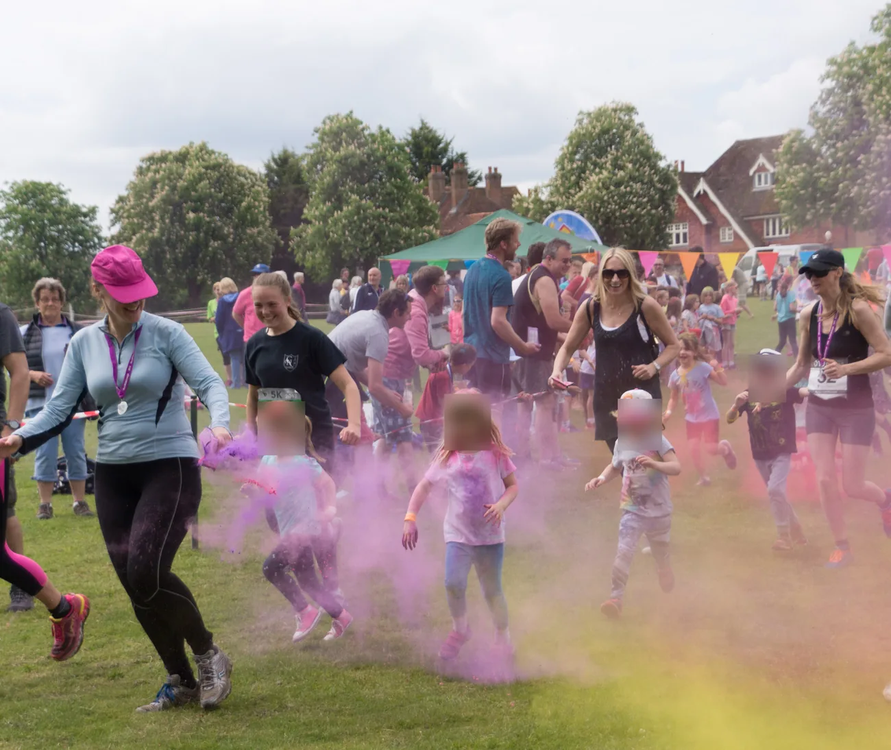 Children running through clouds of pink and yellow colour powder on the Green
