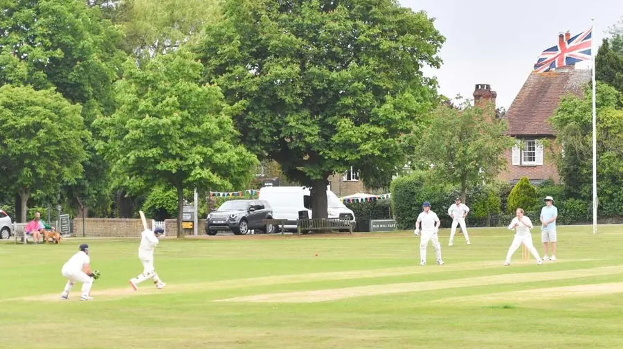 A cricket match in full flow on the Green, the village flag flying beyond